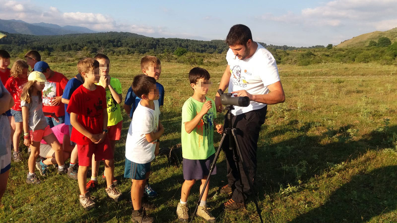 Varios niños miran aves con un telescopio acompañados de un técnico del Proyecto Monachus.