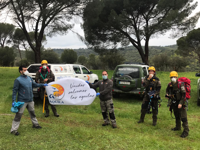 Miembros de GREFA y Agentes Forestales de la Comunidad de Madrid posan junto a cartel del proyecto AQUILA a-LIFE tras la introducción del pollo de águila de Bonelli criado en cautividad en un nido de la Sierra Oeste de Madrid.