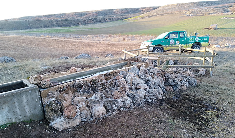 Abrevadero flanqueado por un muro de piedra y charca con cerca de madera construidos para favorecer a la fauna en Valdevarnés (Segovia).