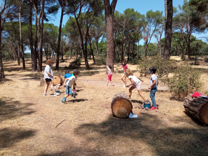 Varios niños y una educadora juegan en plena naturaleza durante nuestros campamentos.
